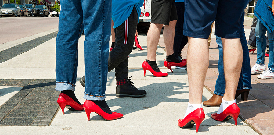 Three pairs of men's legs showing; all with the red heels on the feet.