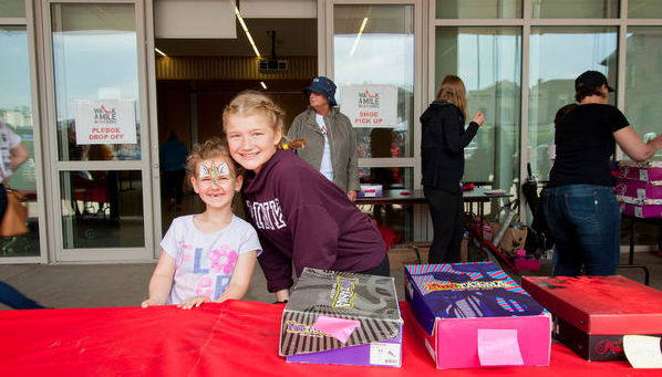 Two young girls smiling at the camera while volunteering to hand out shoes at Walk A Mile In Their Shoes