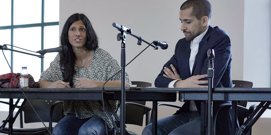 Close-up of Attiya Khan sitting at a table, speaking into a microphone.