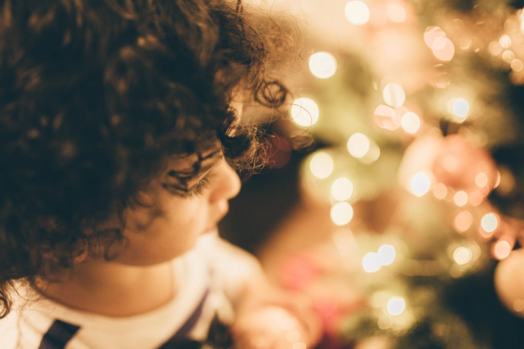 young child sitting in front of a lit Christmas tree