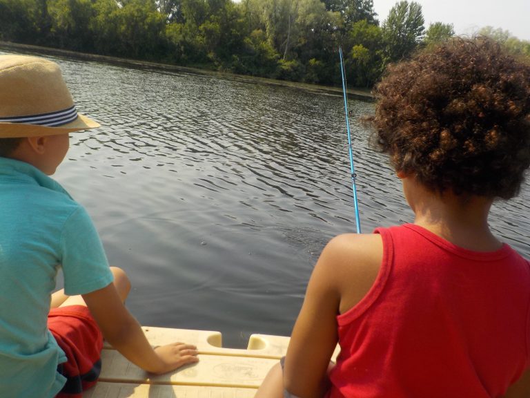 Young children from the back, sitting on a dock, fishing