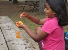 Girl sits at picnic table with hands covered in orange slime